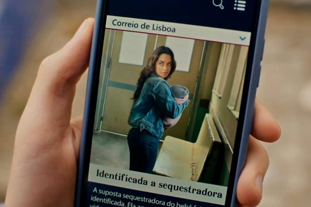 Cell phone screen with mounted image of Brisa (Lucy Alves) holding a baby, as reported in a Portuguese newspaper