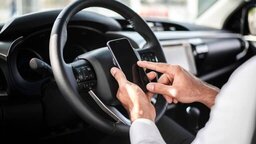 Driver immersed in traffic, with his hands on the steering wheel and using his cell phone, while the blurred background highlights the urban scene