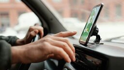 Hands on the steering wheel and on the cell phone, interacting with a transportation app while the car is parked, reflecting the practical use of the app